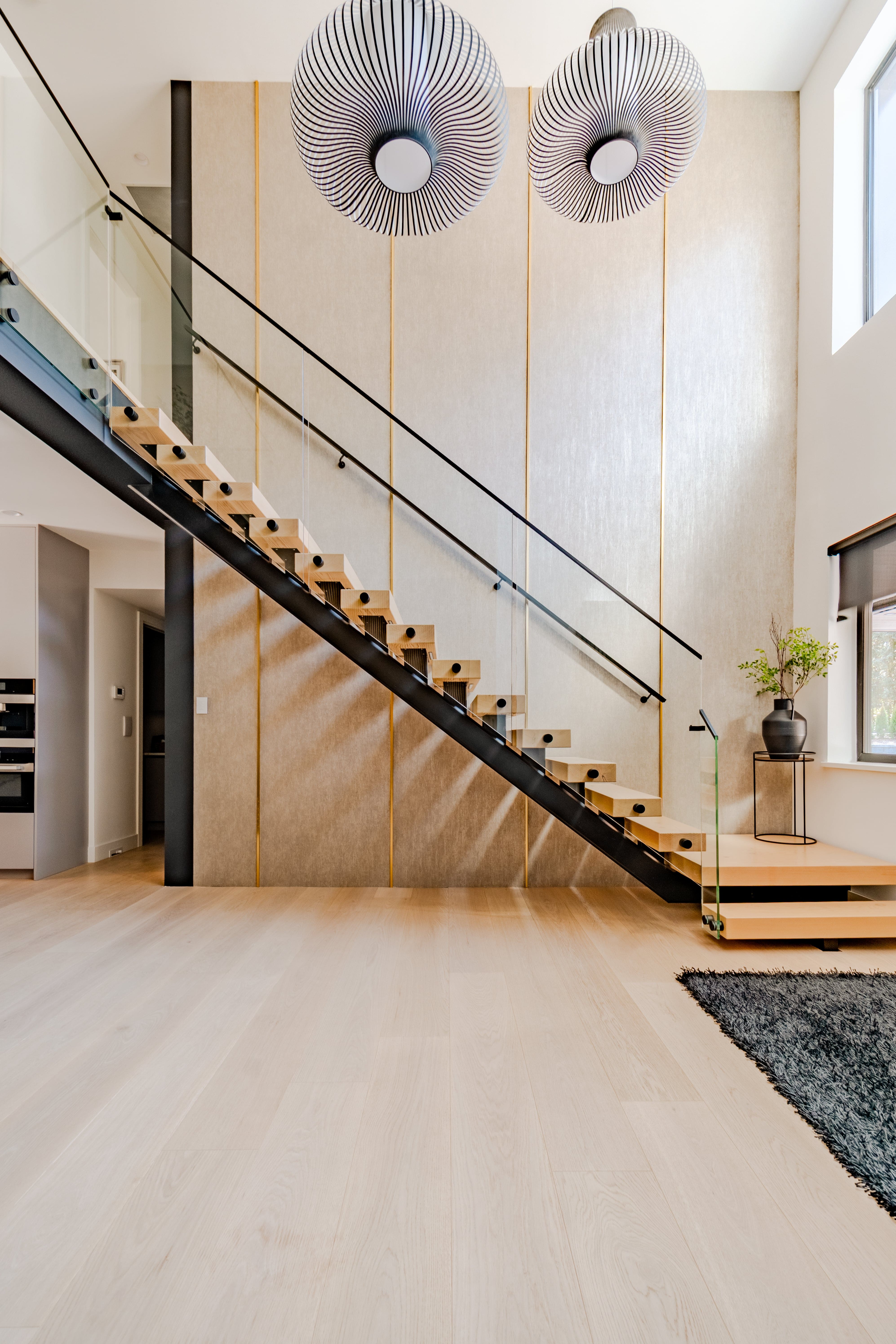 Luxury home foyer real estate photography Vancouver — floating open-tread staircase with black steel stringer and glass railing, double Vertigo pendant lights, double-height ceilings, and wide-plank oak floors