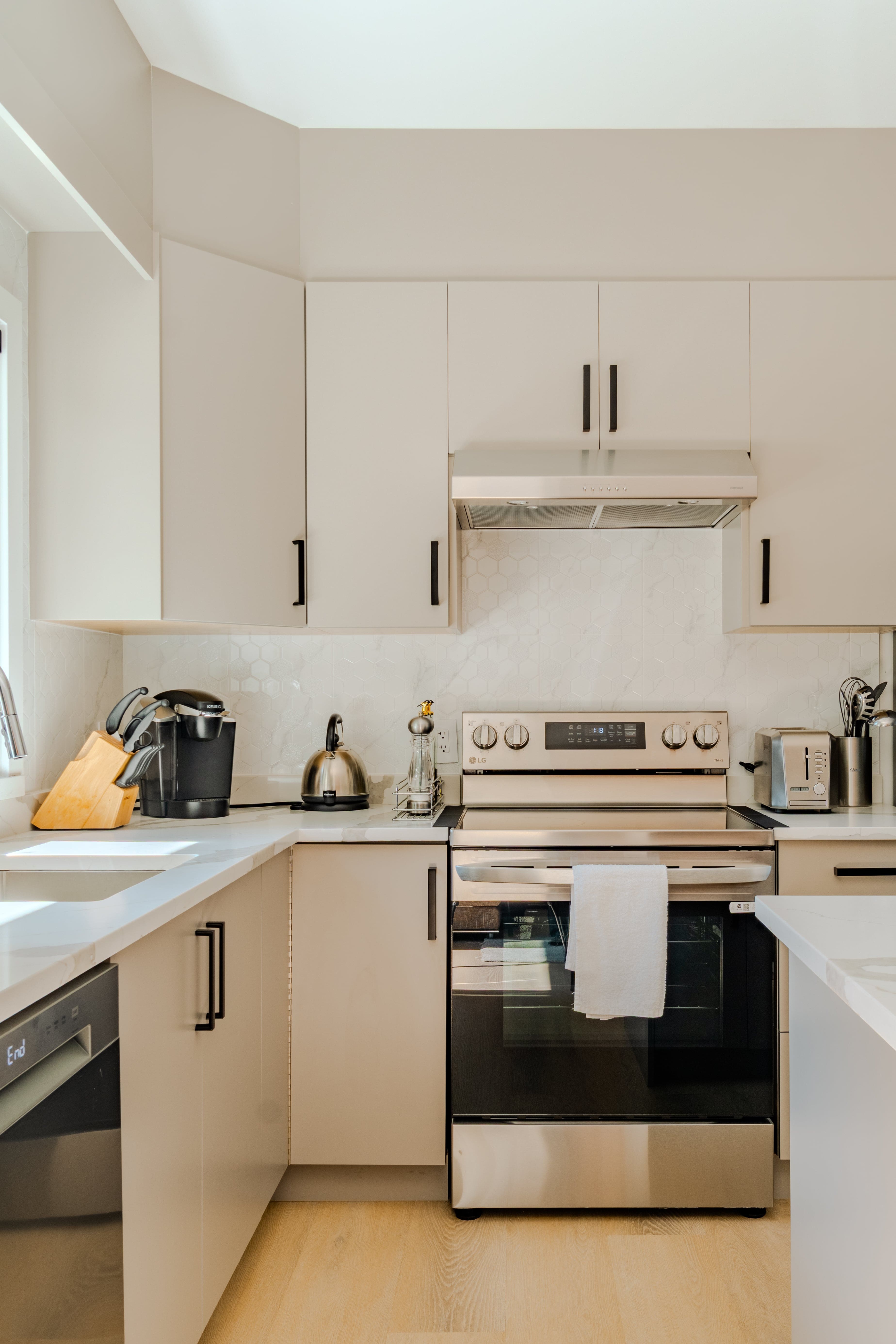 Modern kitchen real estate photography Vancouver — cream flat-front cabinetry with matte black hardware, white quartz countertops, marble-look tile backsplash, and stainless steel appliances