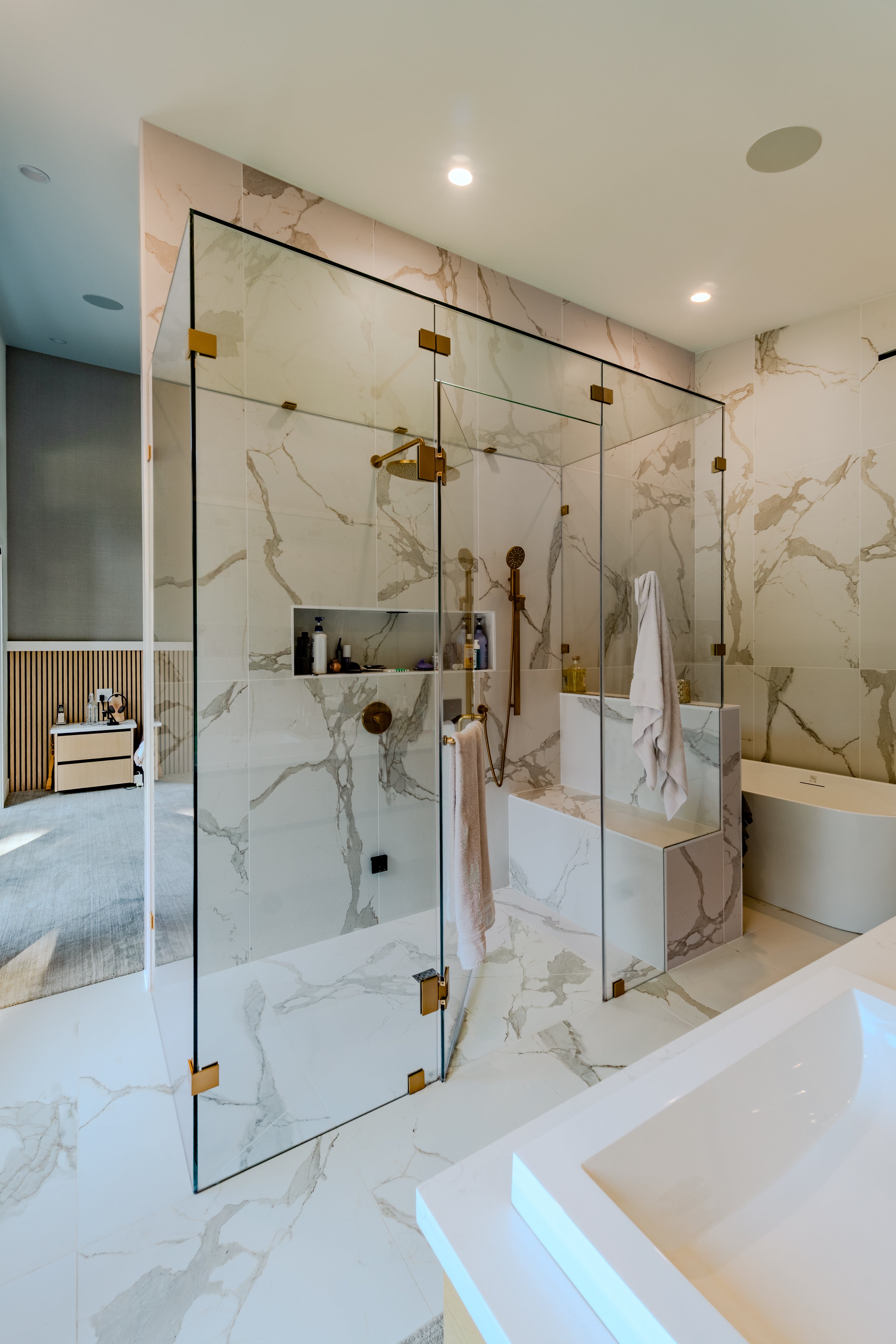 Luxury ensuite real estate photography Vancouver — full-height book-matched Calacatta marble tile, frameless glass shower enclosure with brushed gold hardware, integrated marble bench, and undermount tub