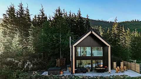A-frame home exterior with a deck and fire pit surrounded by forest