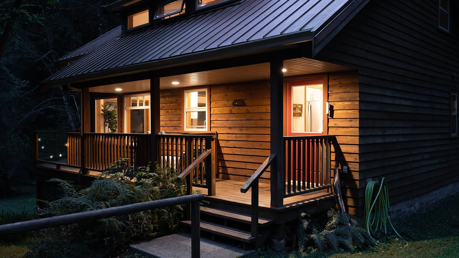 Cabin porch lit at dusk, warm light through the windows